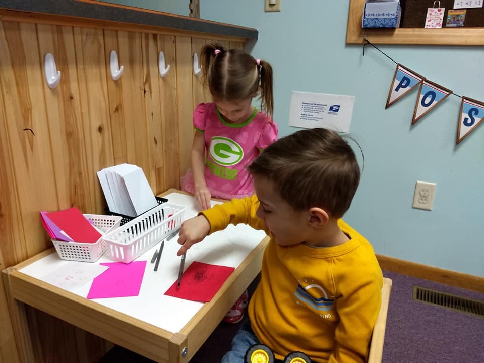 Two children playing at a small table with paper and writing tools
