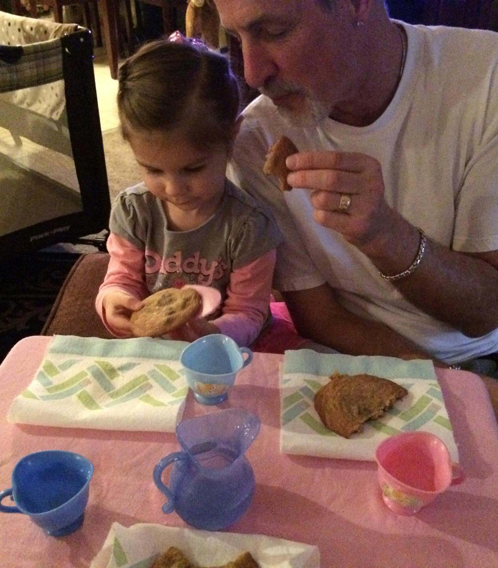 Adult and child eating cookies at a small table with toy tea set