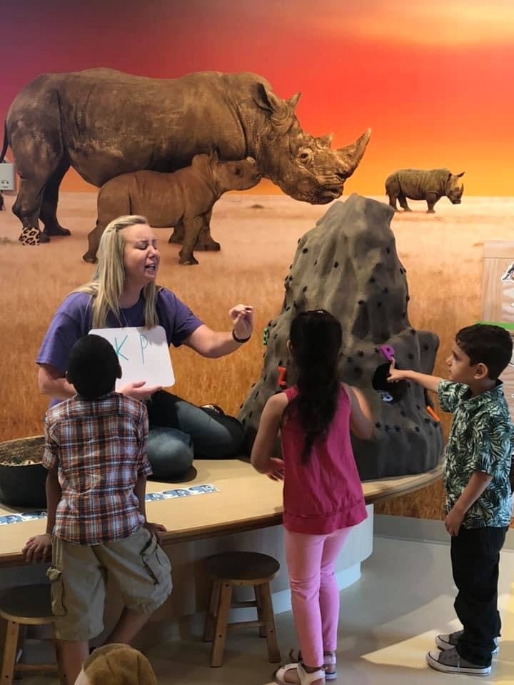 Adult teaching children in front of a rhinoceros mural