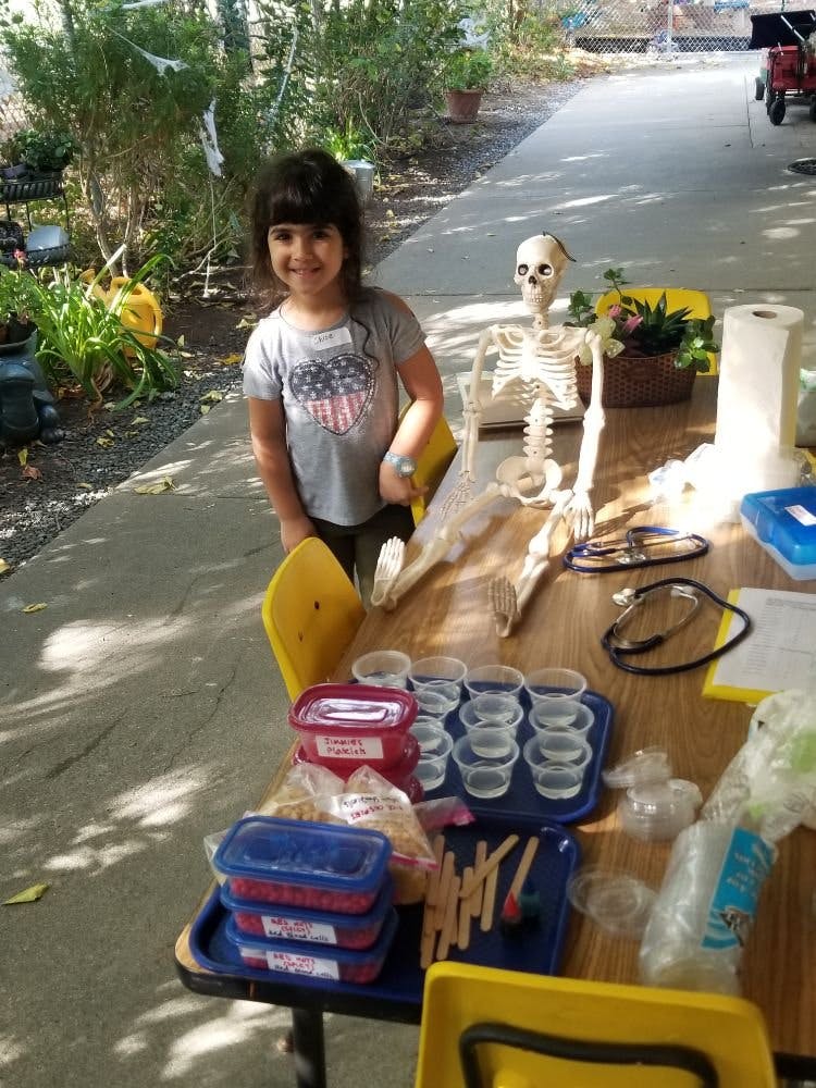 Child standing next to a skeleton sitting at a table with craft supplies