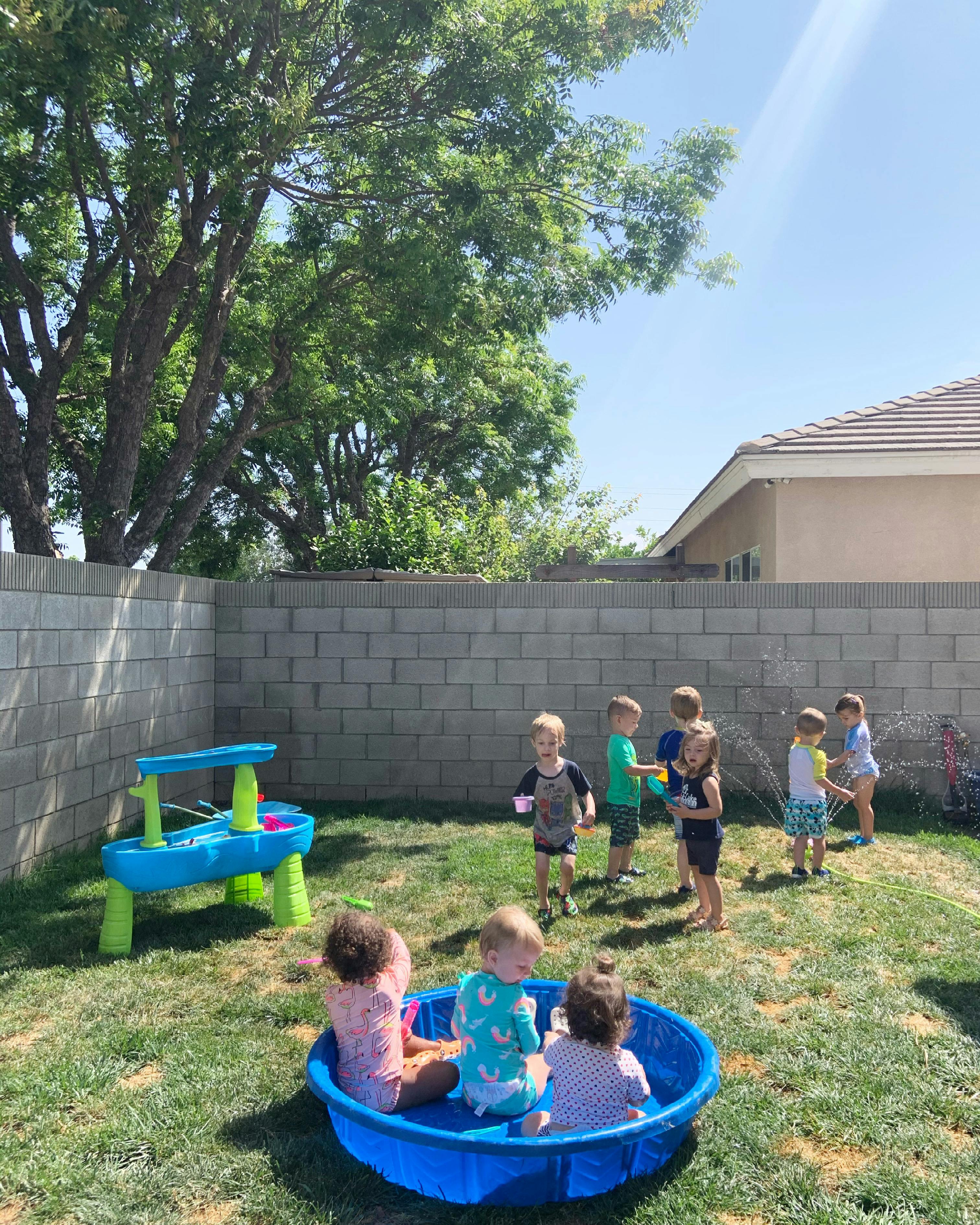 Children playing in a backyard with a small pool and sprinkler