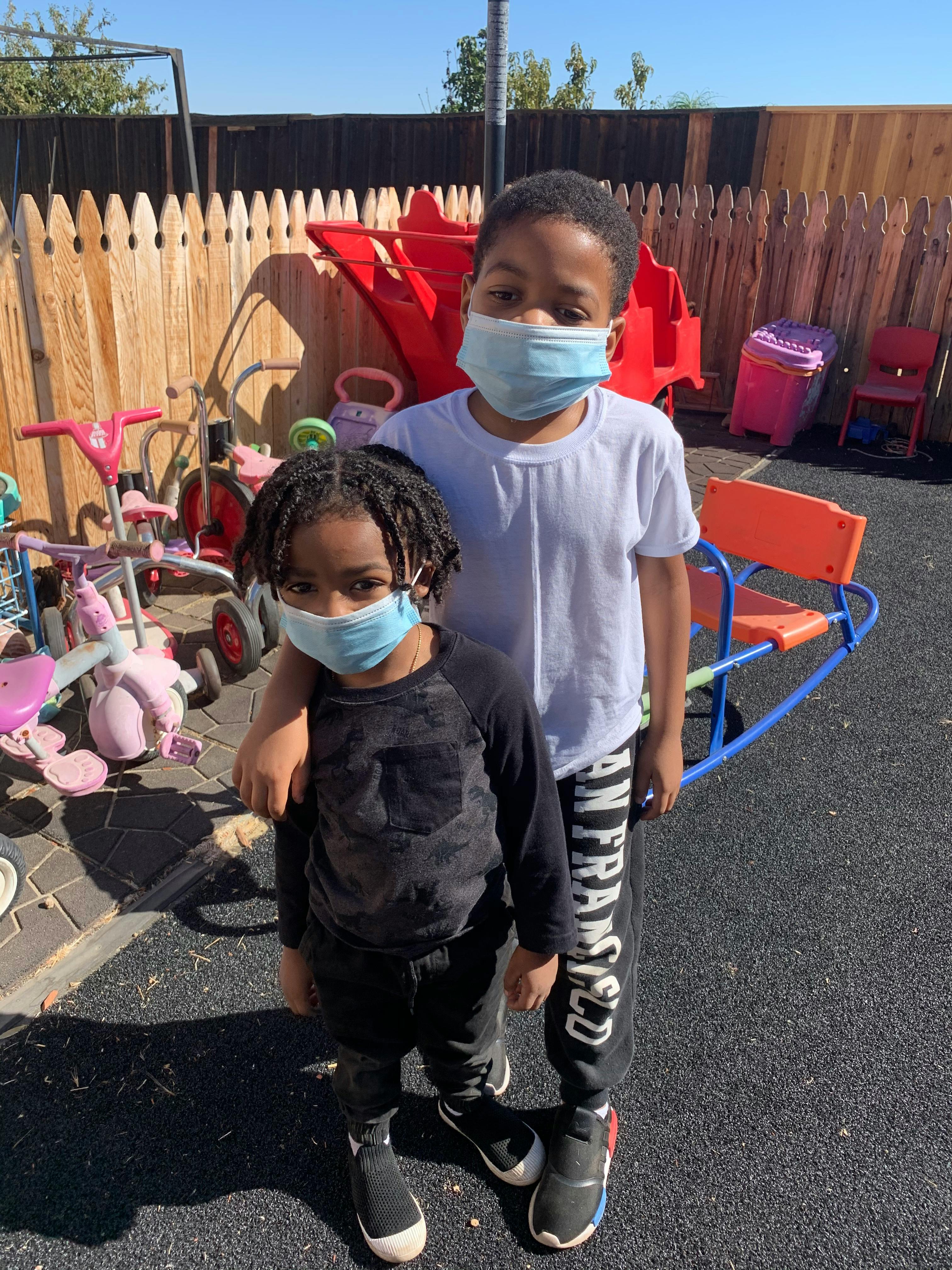 Two children wearing face masks standing together outdoors