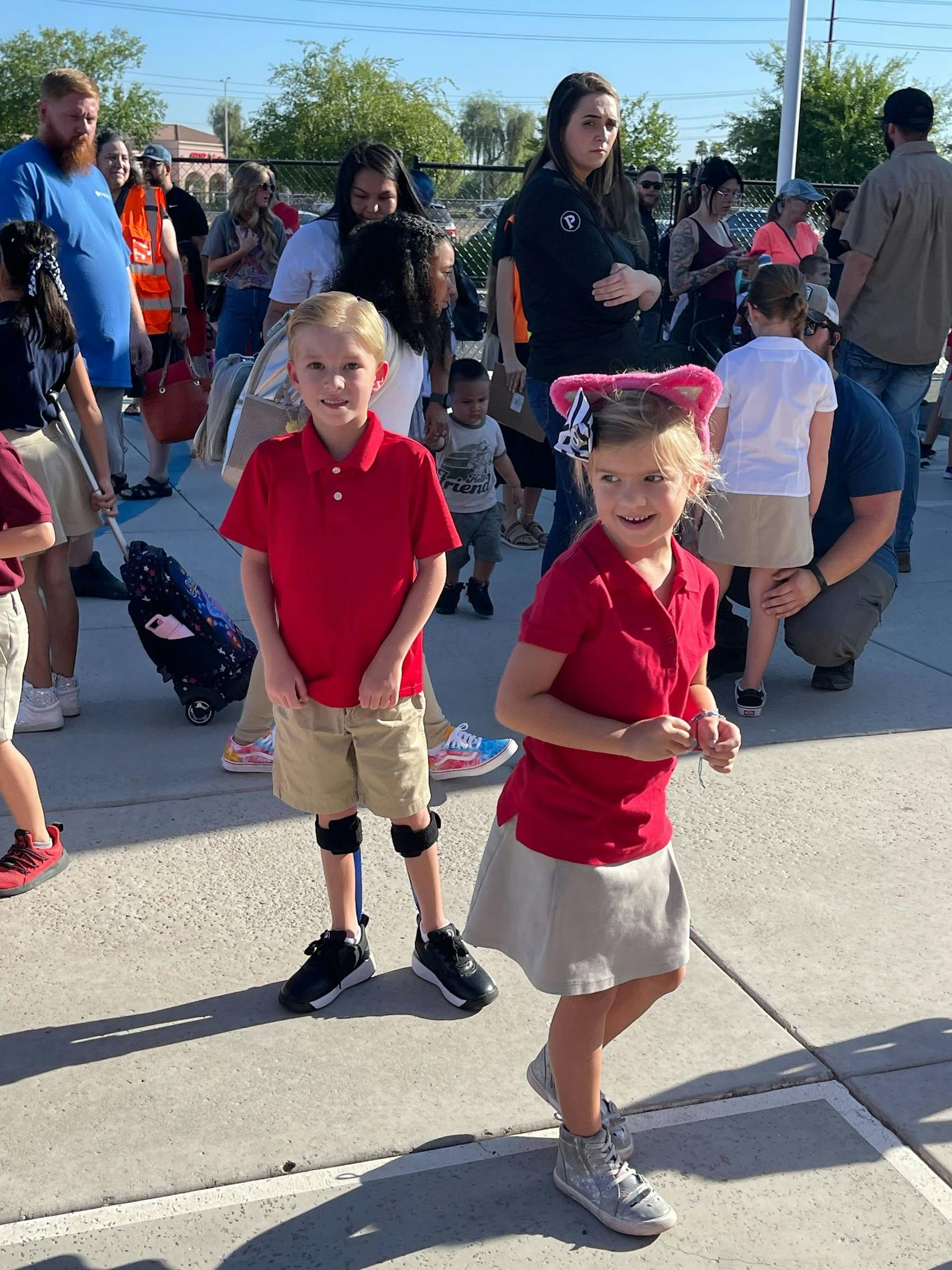 Two children in red shirts and khaki bottoms standing outdoors