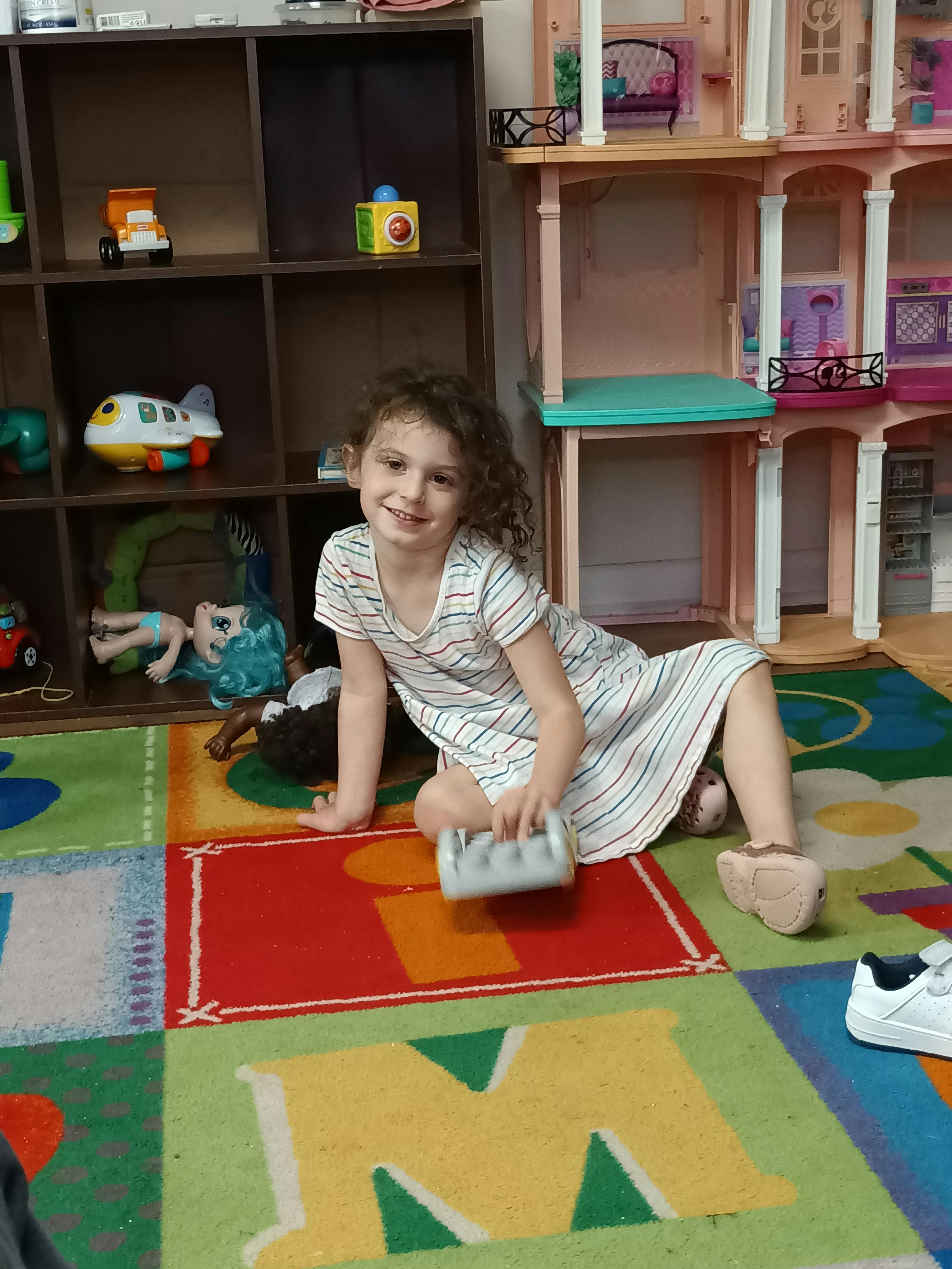 Child sitting on a colorful rug with toys and a dollhouse in the background