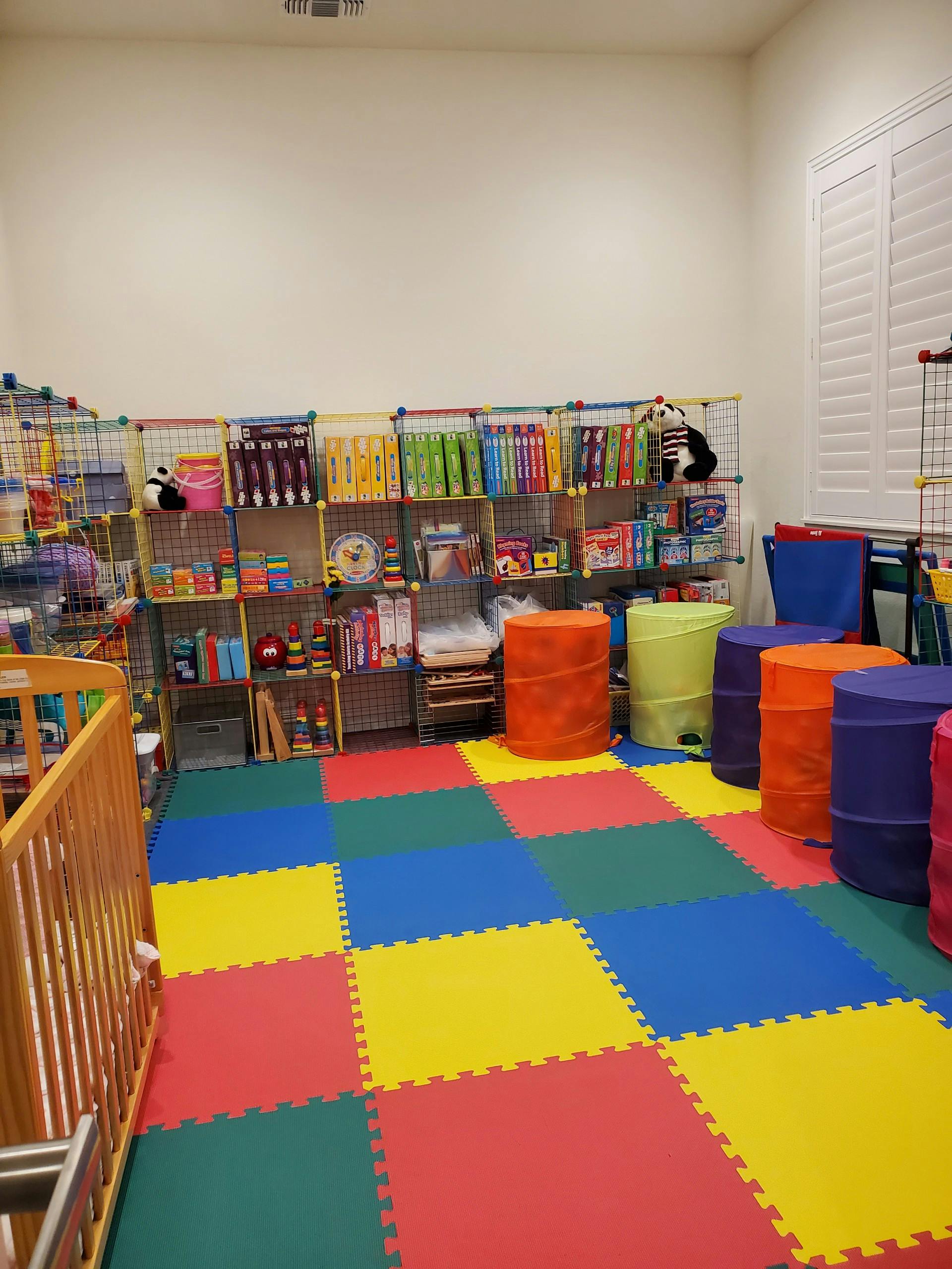 Playroom with colorful floor mats, shelves of books and toys, and soft barrels