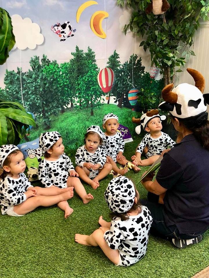 Adult in cow hat reading to children in cow print outfits