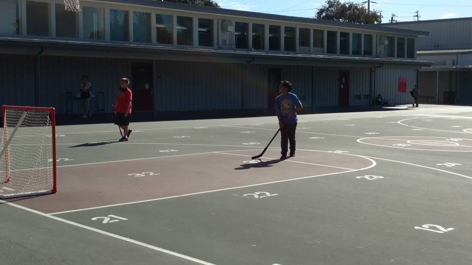 Two people playing hockey on an outdoor court