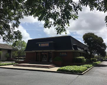 Brick building with a dark roof and a sign that says "Sunstate"