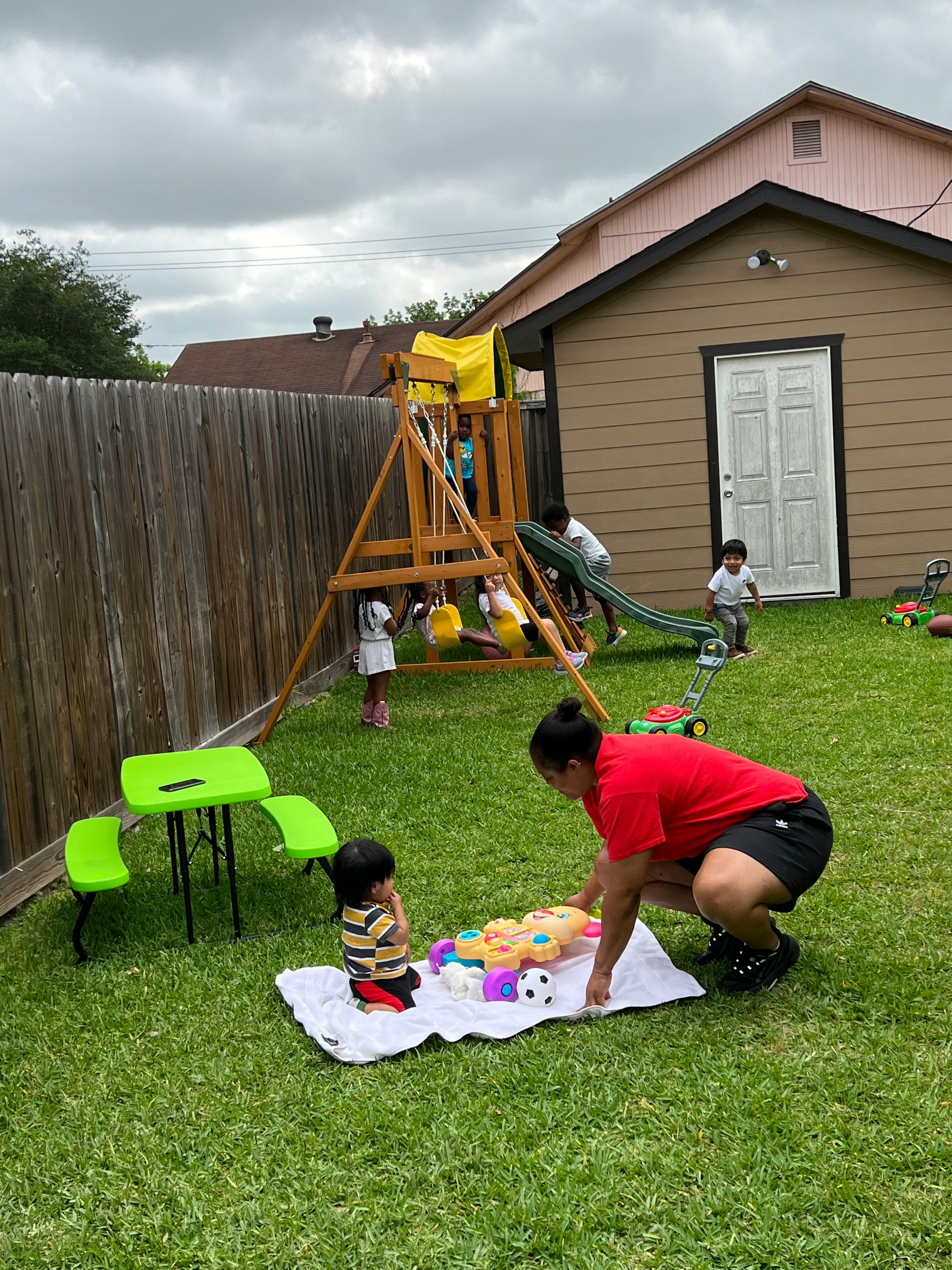 Person and child playing with toys on a blanket in a yard