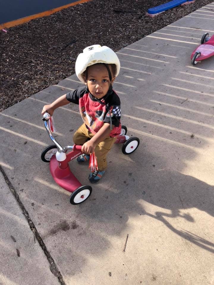 Child wearing a helmet and riding a tricycle on a red tricycle
