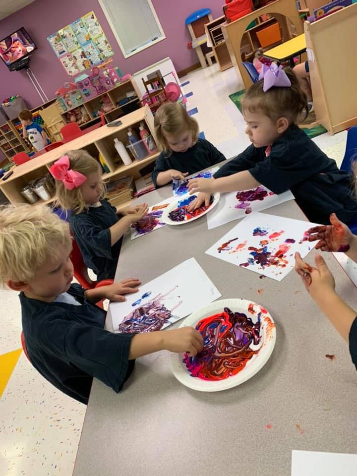 Children finger painting at a table in a classroom