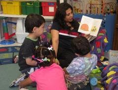 Adult reading a book to three children in a classroom