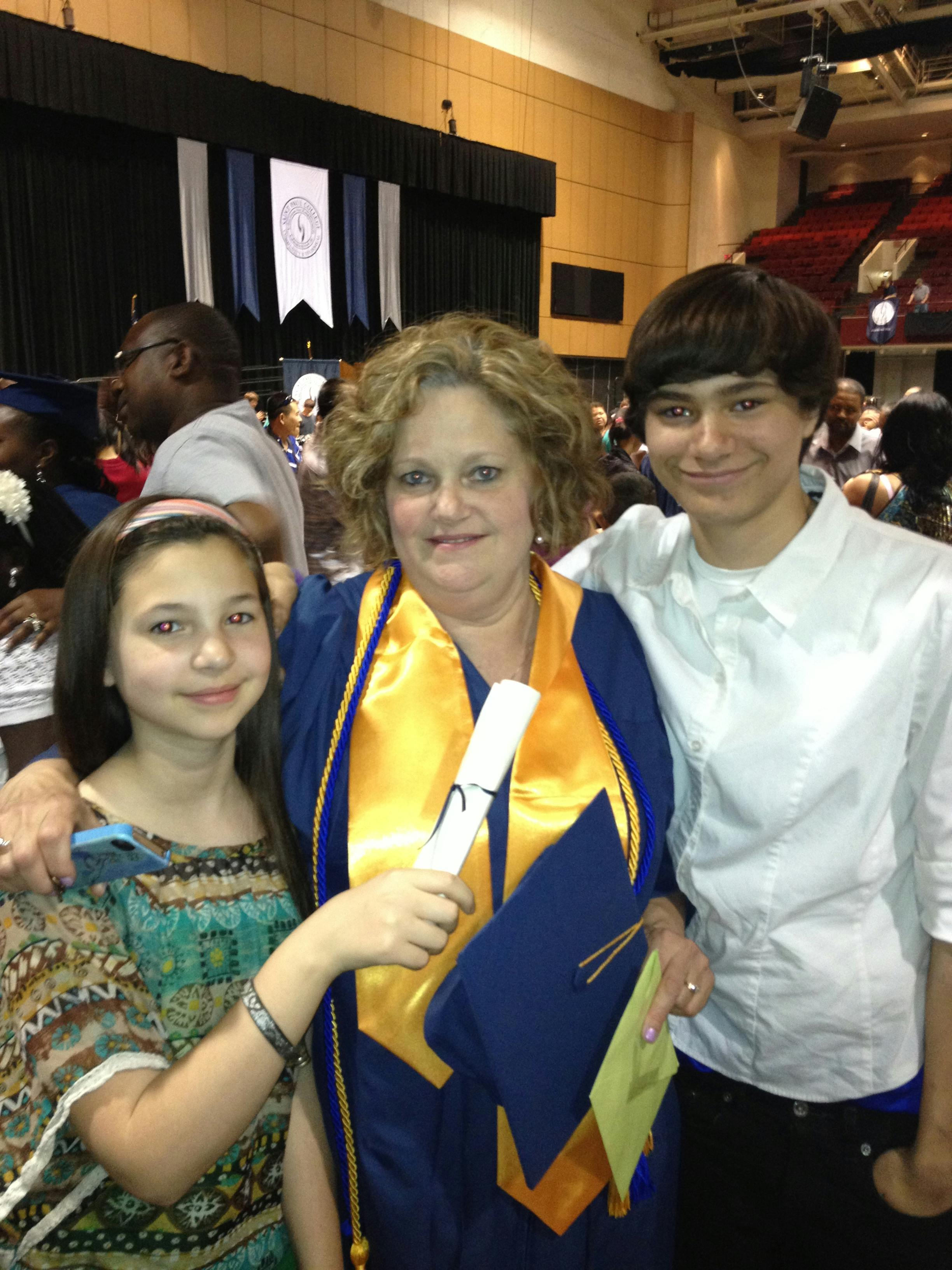 Person in graduation gown holding diploma with two children
