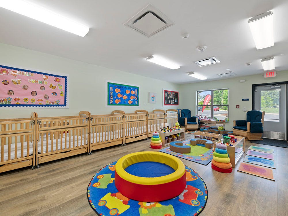 Cribs and play area inside a brightly lit childcare classroom