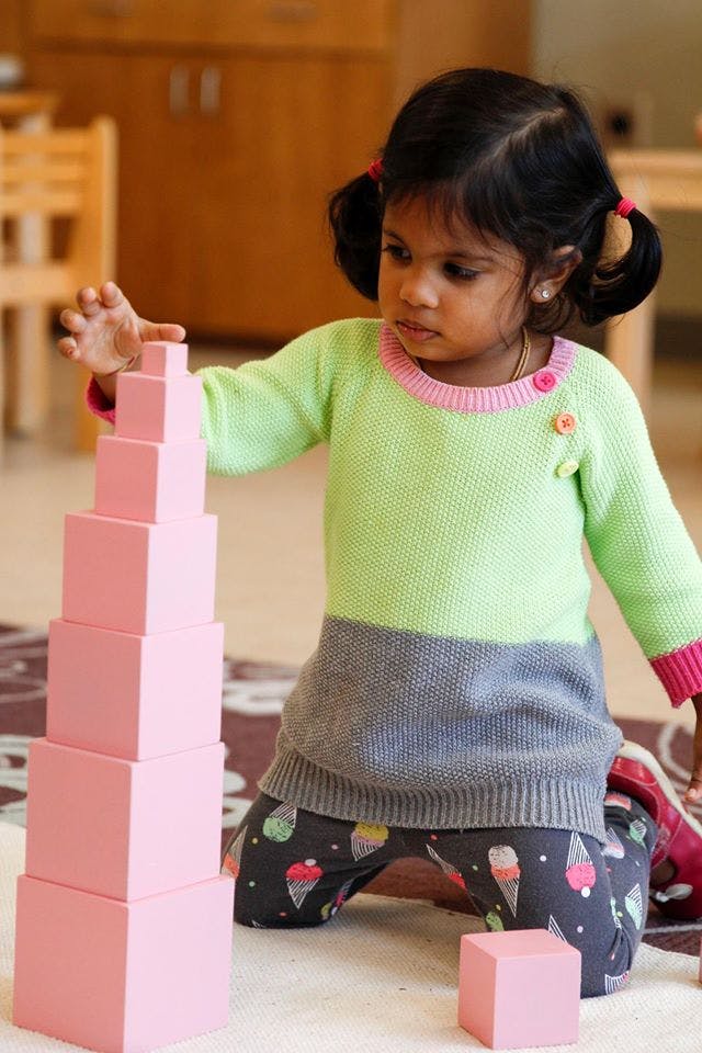 Child kneeling and stacking pink blocks