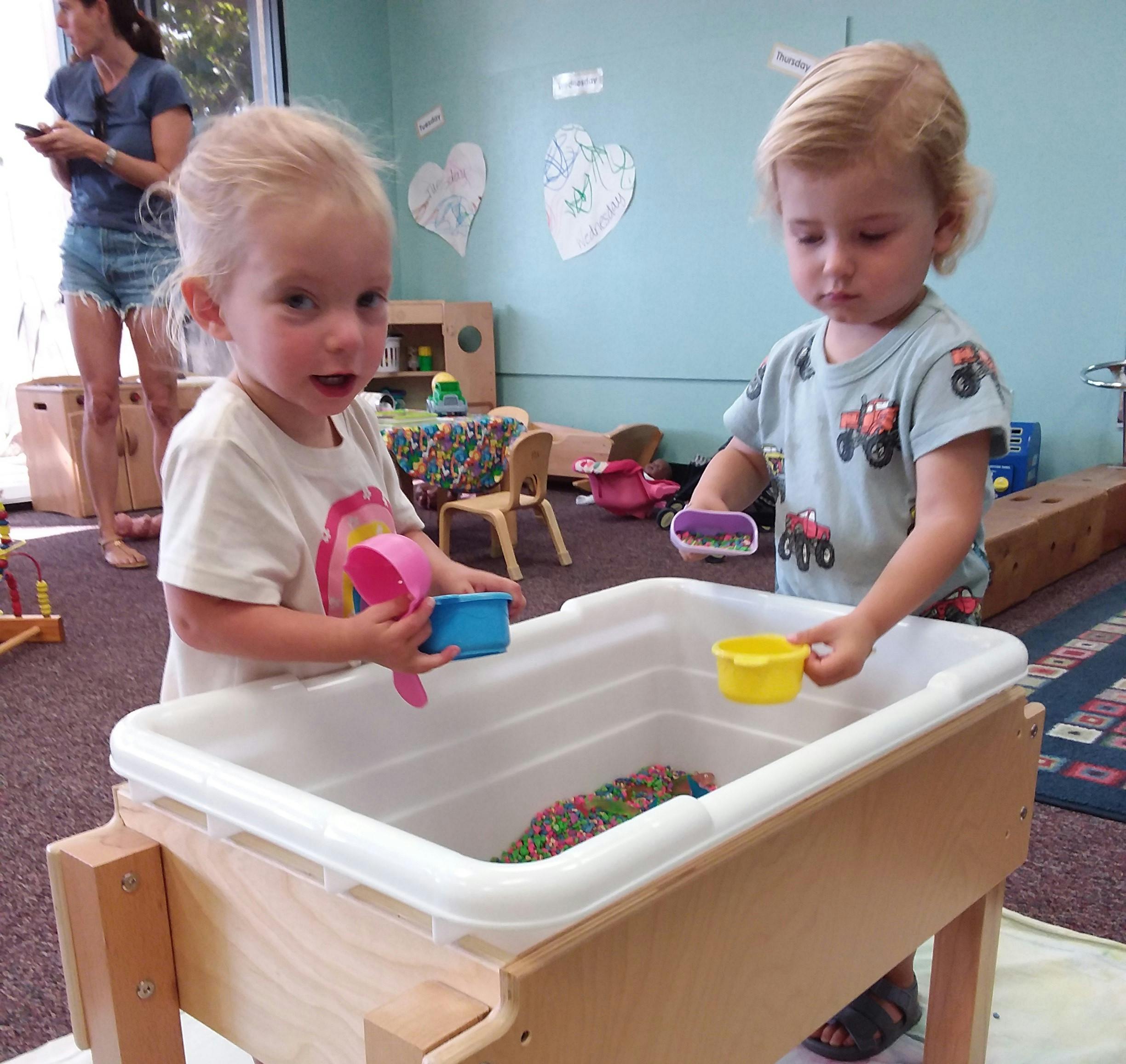 Two children playing with toys in a sensory bin in a classroom