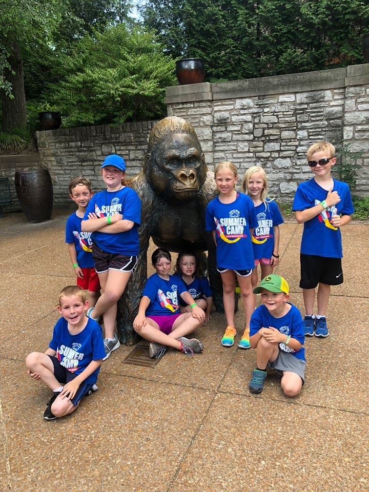 Children in blue shirts posing with a gorilla statue