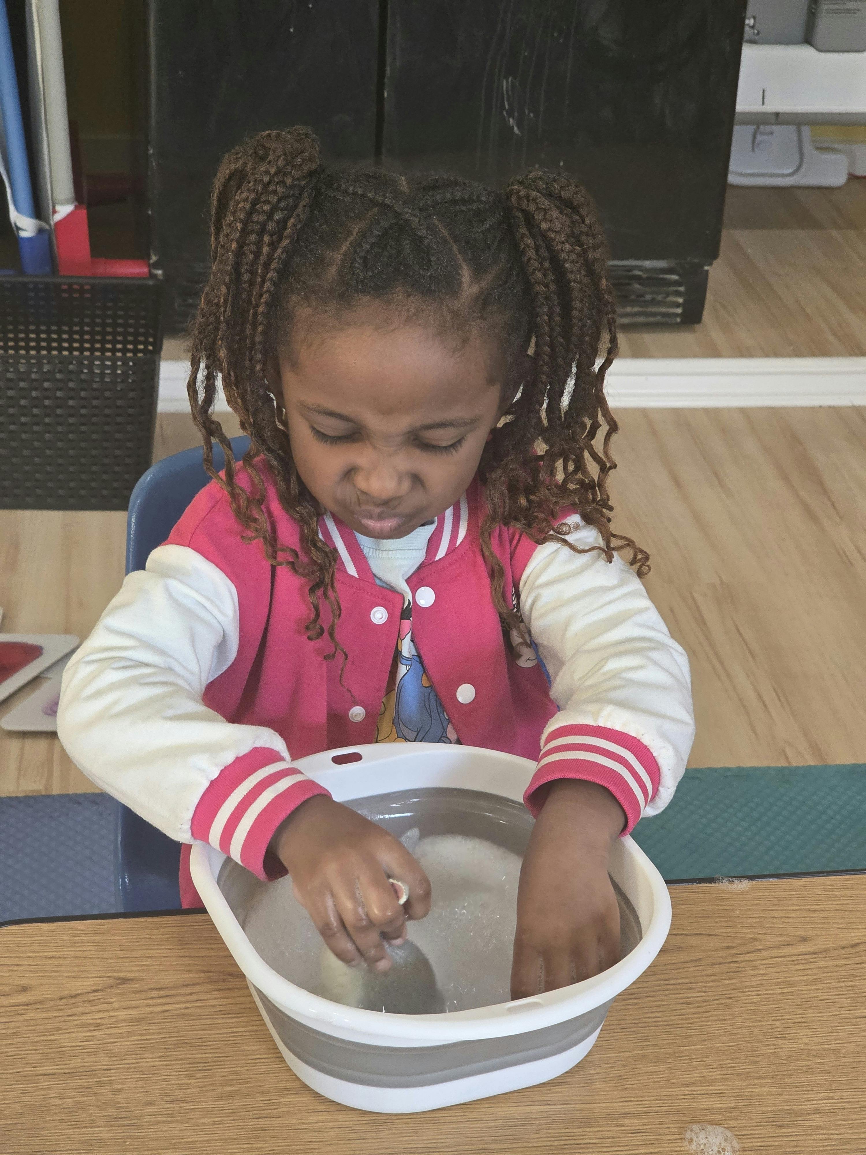 Child with braided hair playing with water in a basin
