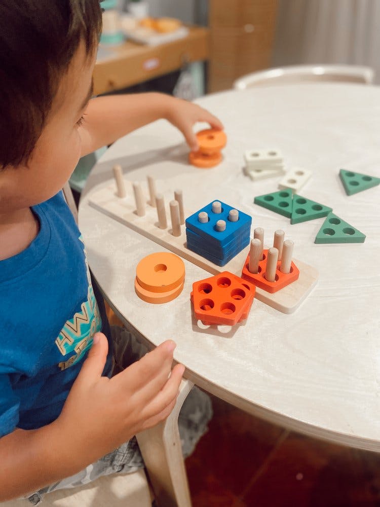 Child playing with a wooden shape sorter toy on a table