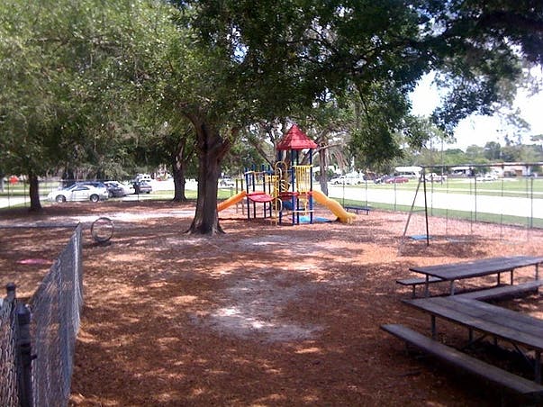 Playground with slides, swings, and picnic tables under trees