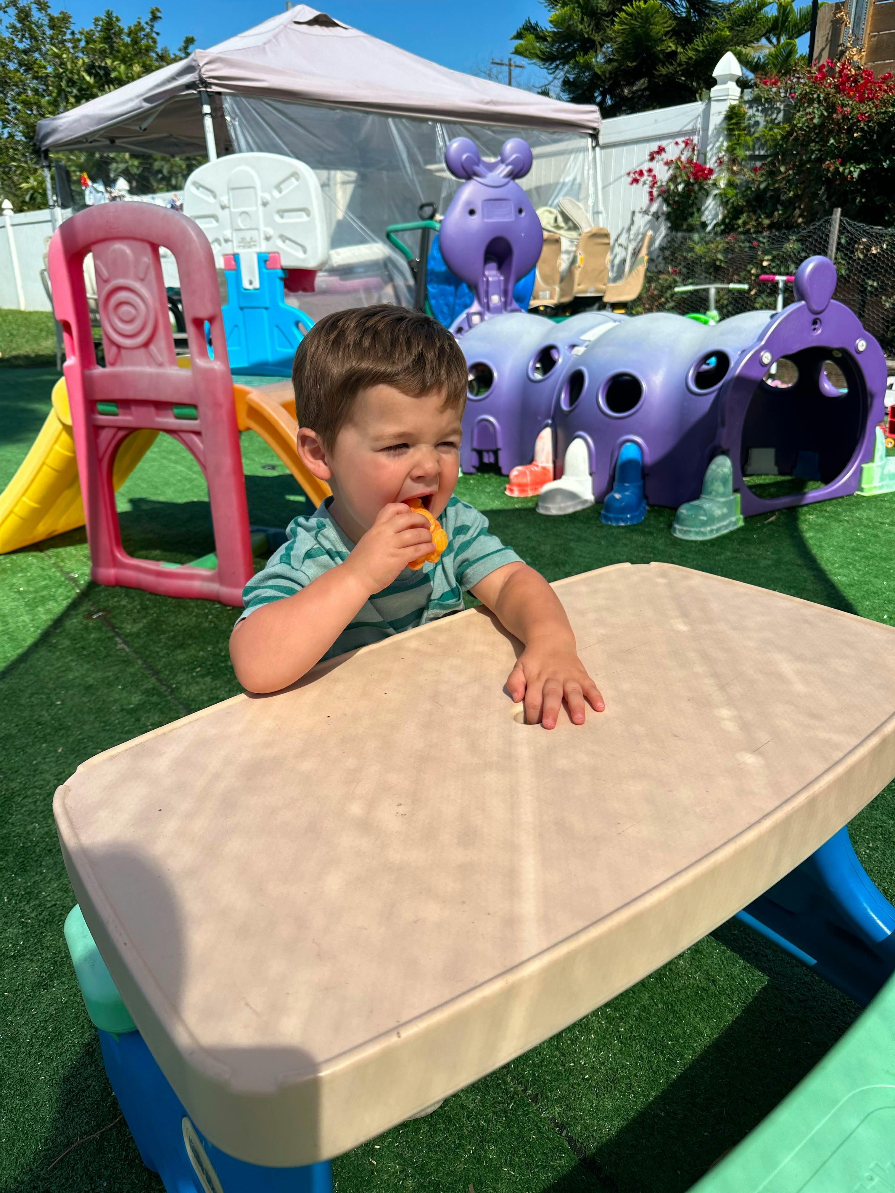 Child eating an orange snack at a small plastic table on a playground