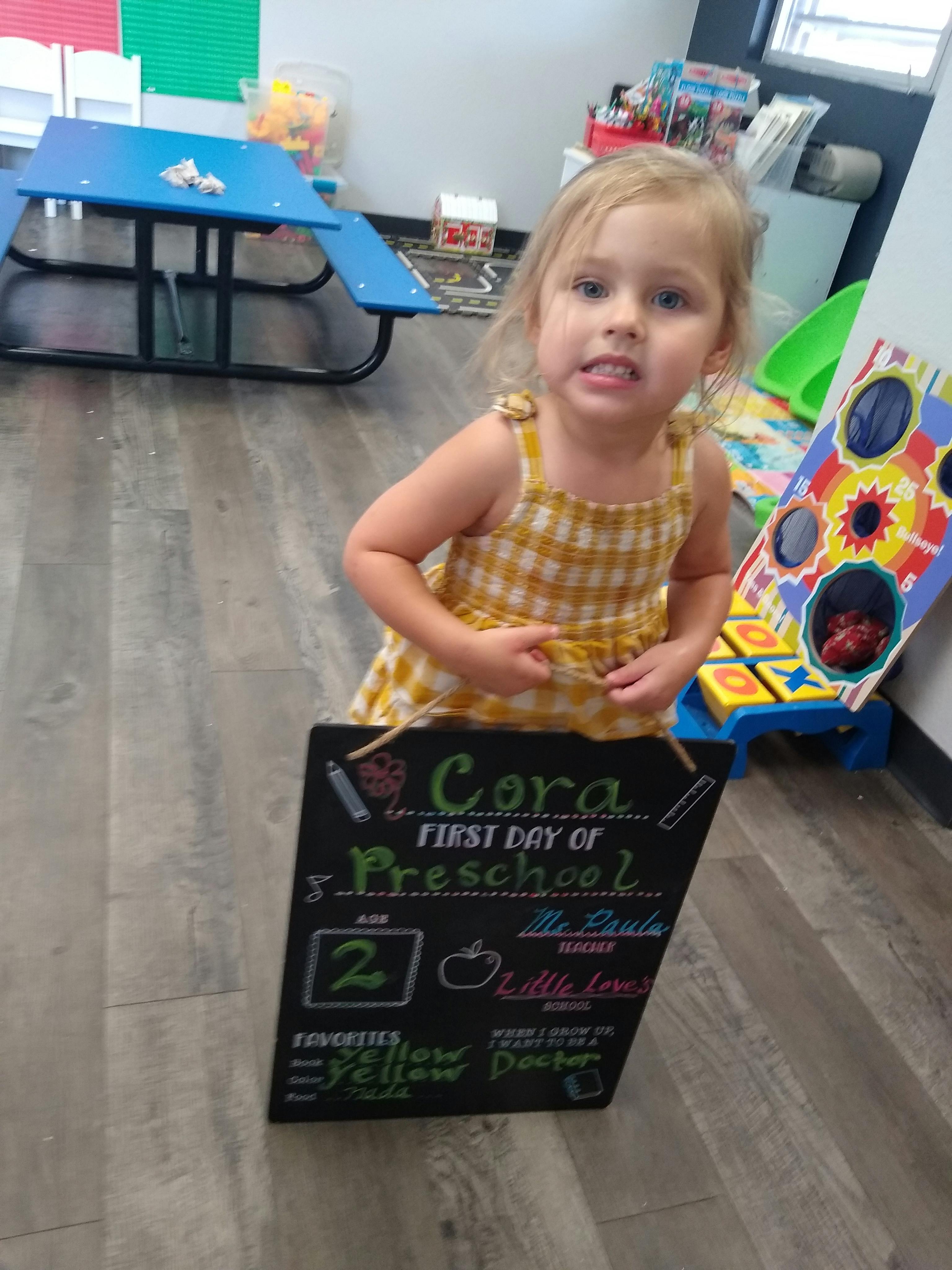 Child holding a first day of preschool chalkboard sign