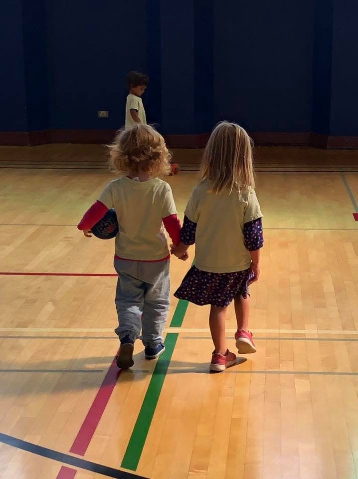 Two children holding hands and walking on a gym floor