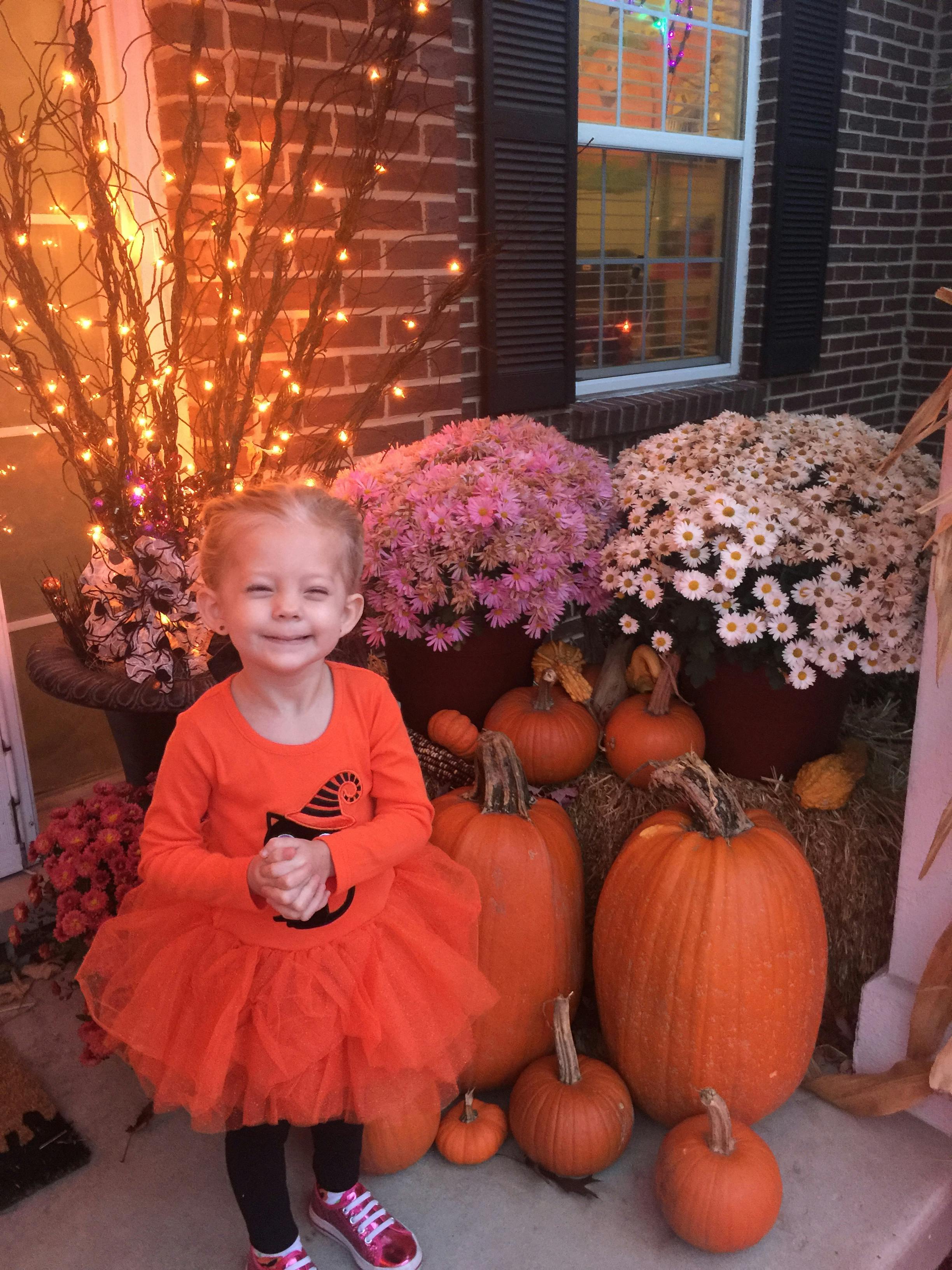Child in orange dress standing among pumpkins and mums