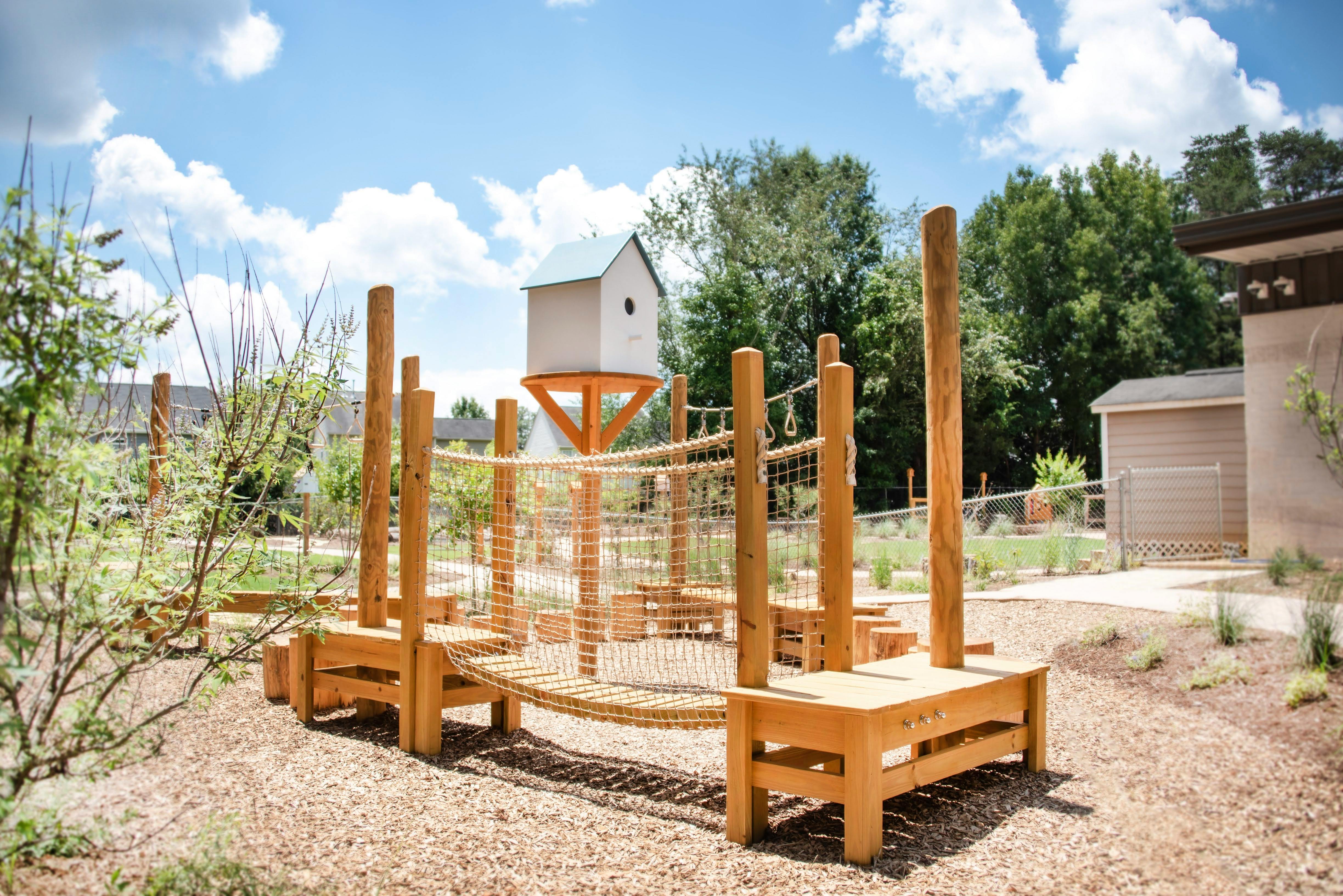 Wooden playground structure with rope netting and a small house on stilts