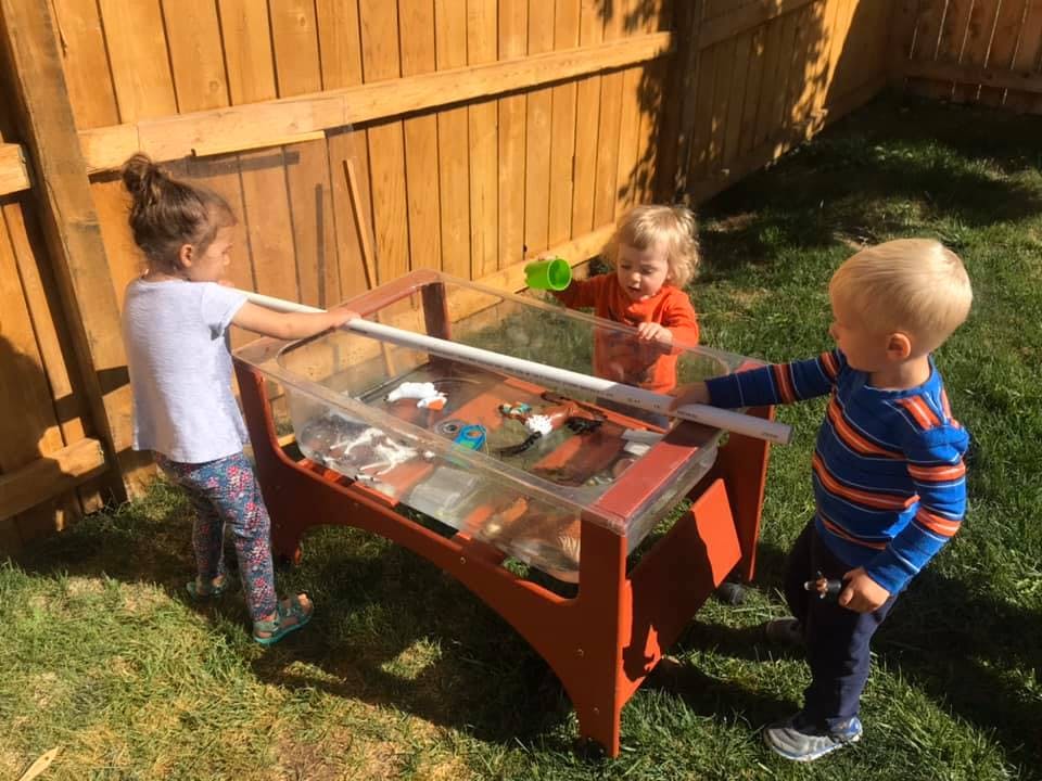 Three children playing at a water table outdoors