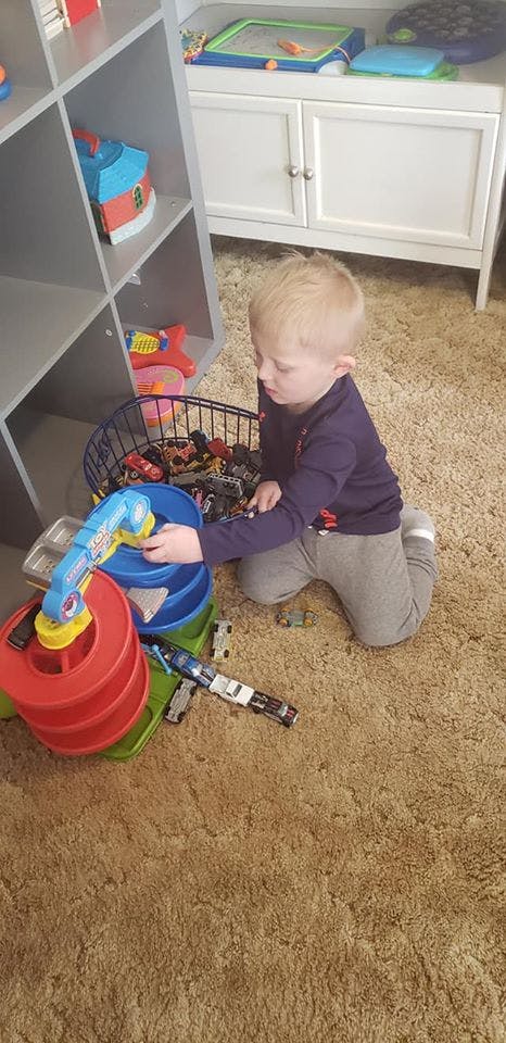 Child kneeling on carpet playing with toy cars and a toy garage