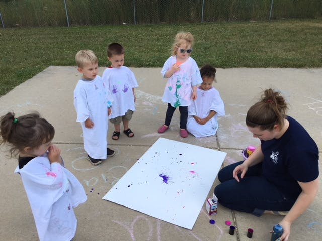 Adult and children painting on a large white board outdoors