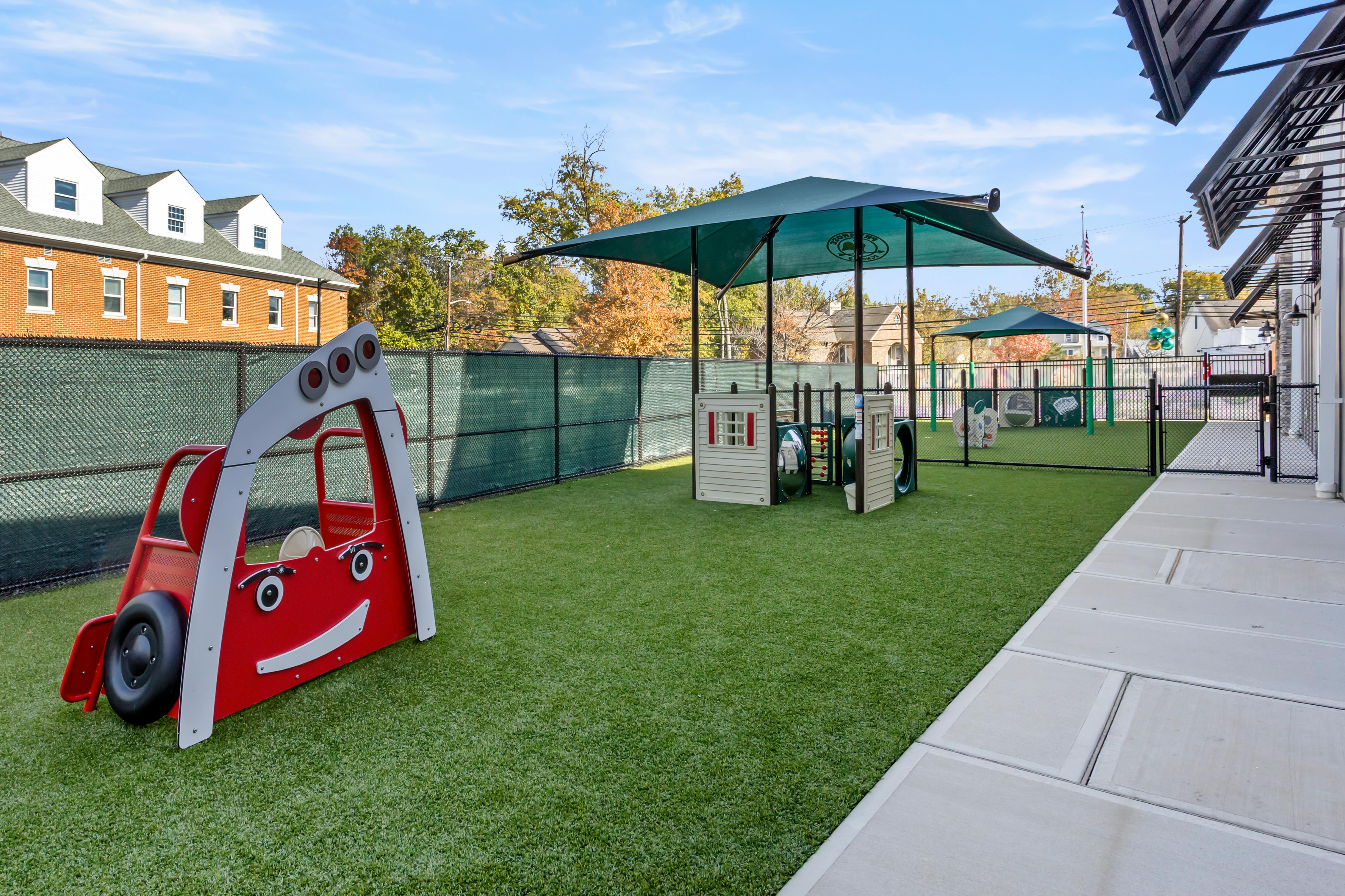 Outdoor playground with red car, climbing structure, and green shade covers