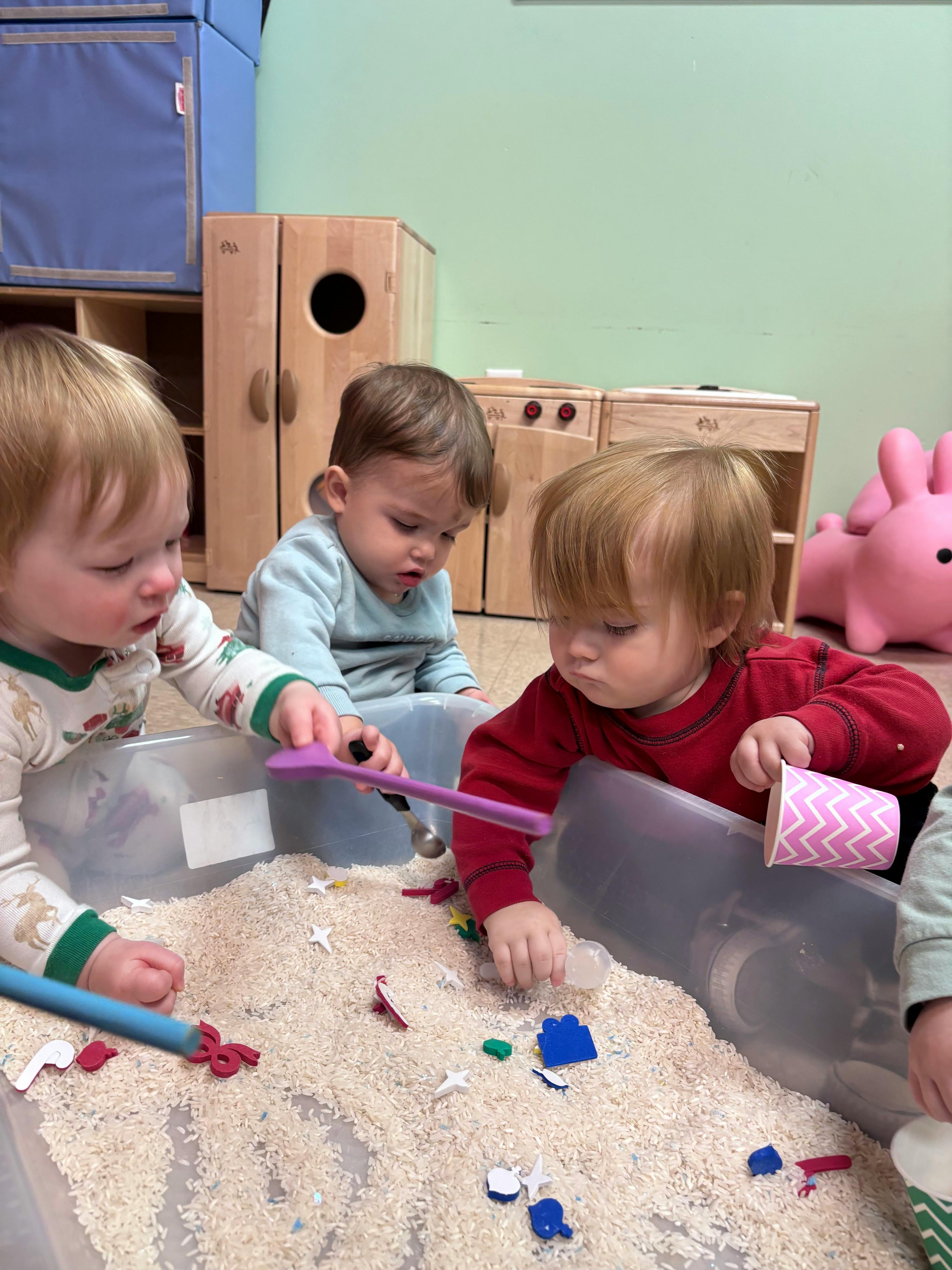 Three children playing with rice and small objects in a container