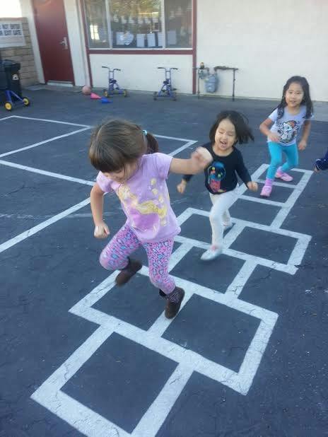 Three children playing hopscotch on a paved surface