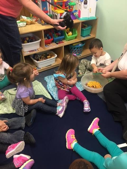 Adult holding a camera over children sitting on the floor