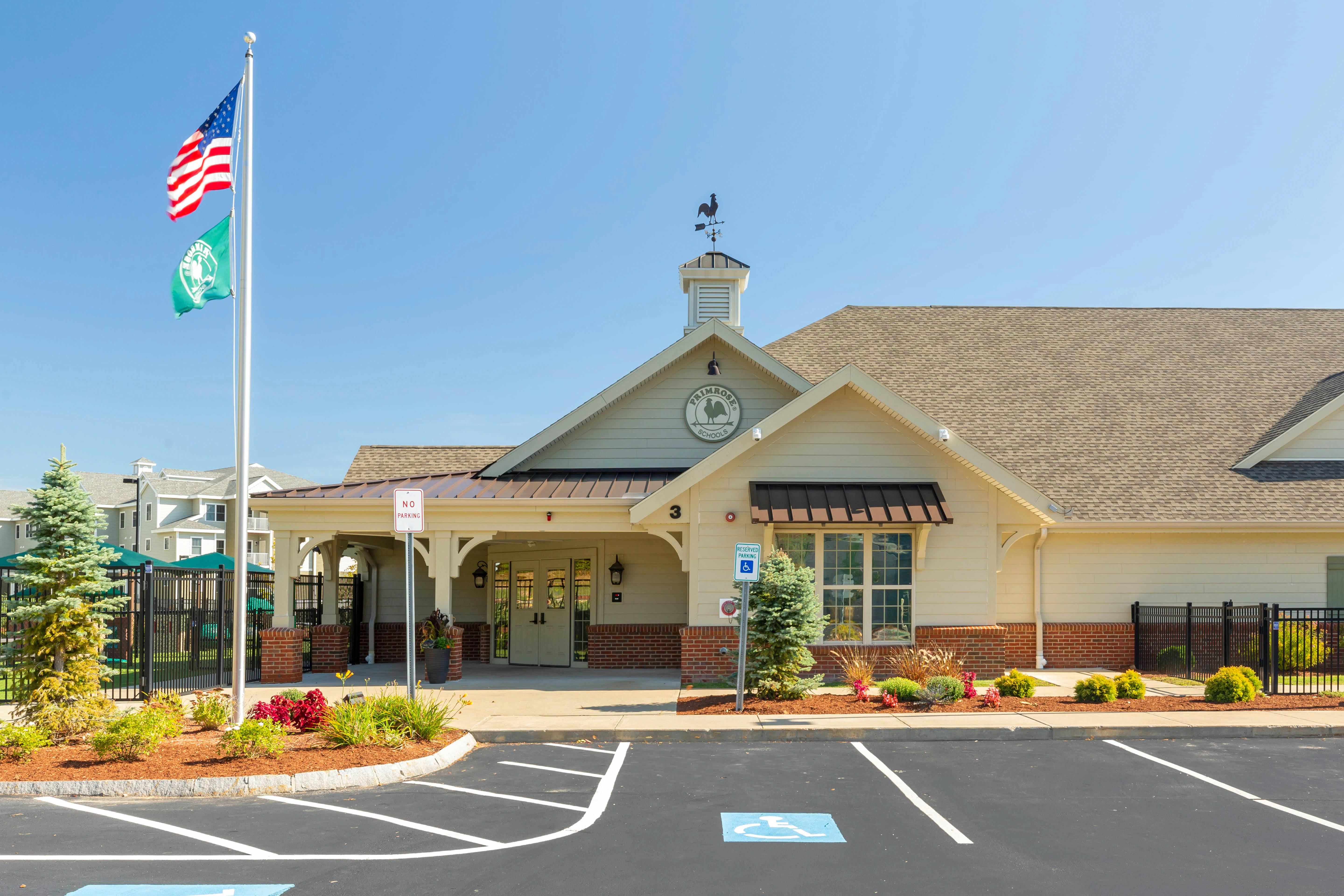 Exterior of a building with "Primrose Schools" sign, US flag, and green flag