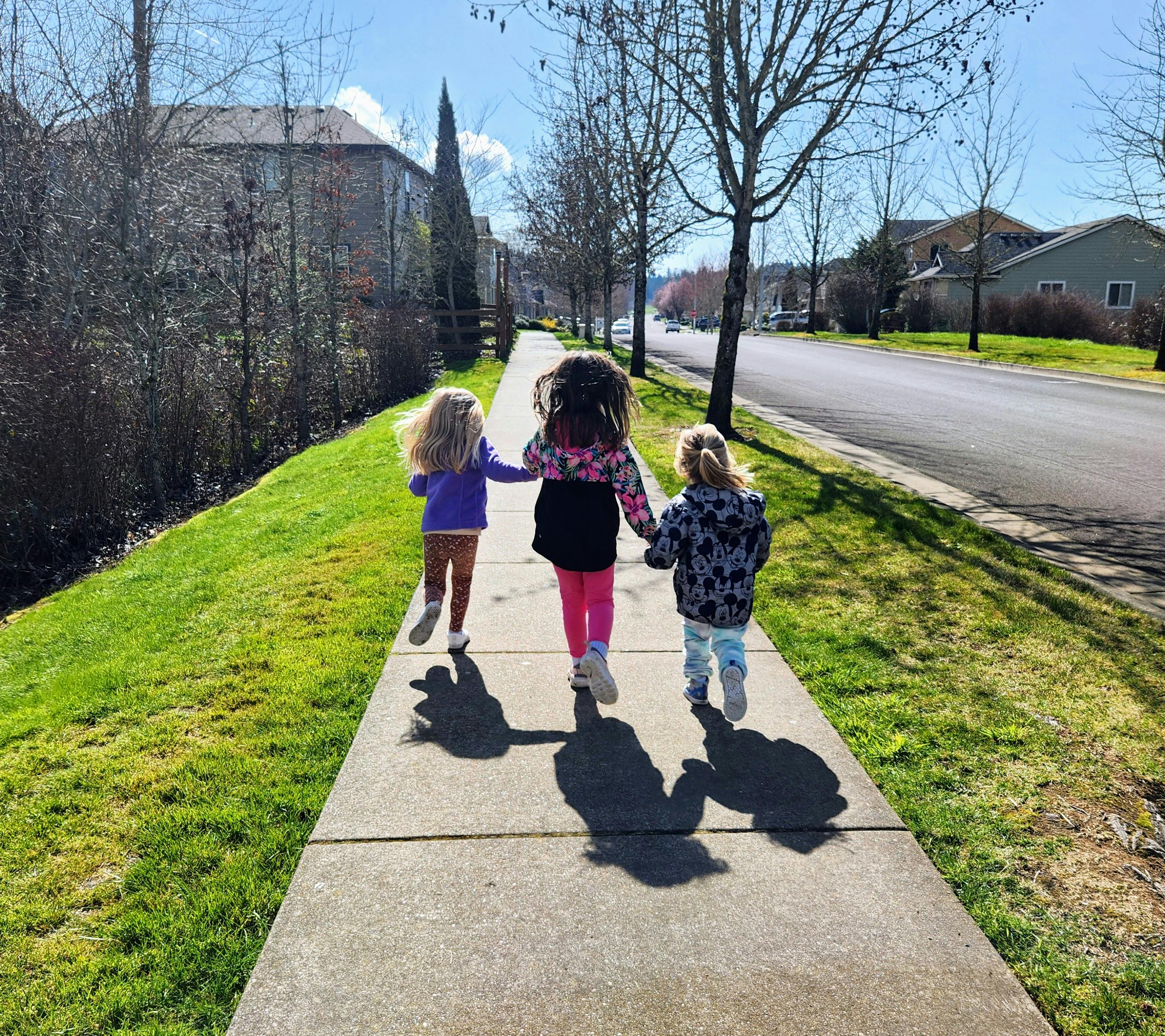 Three children walking on a sidewalk