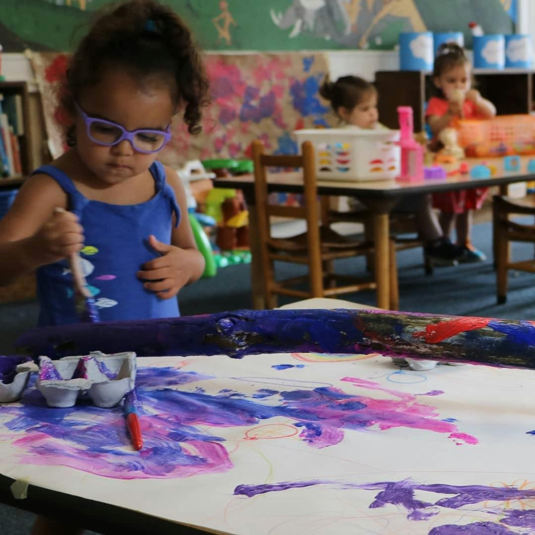 Child in glasses painting a wooden stick in a classroom