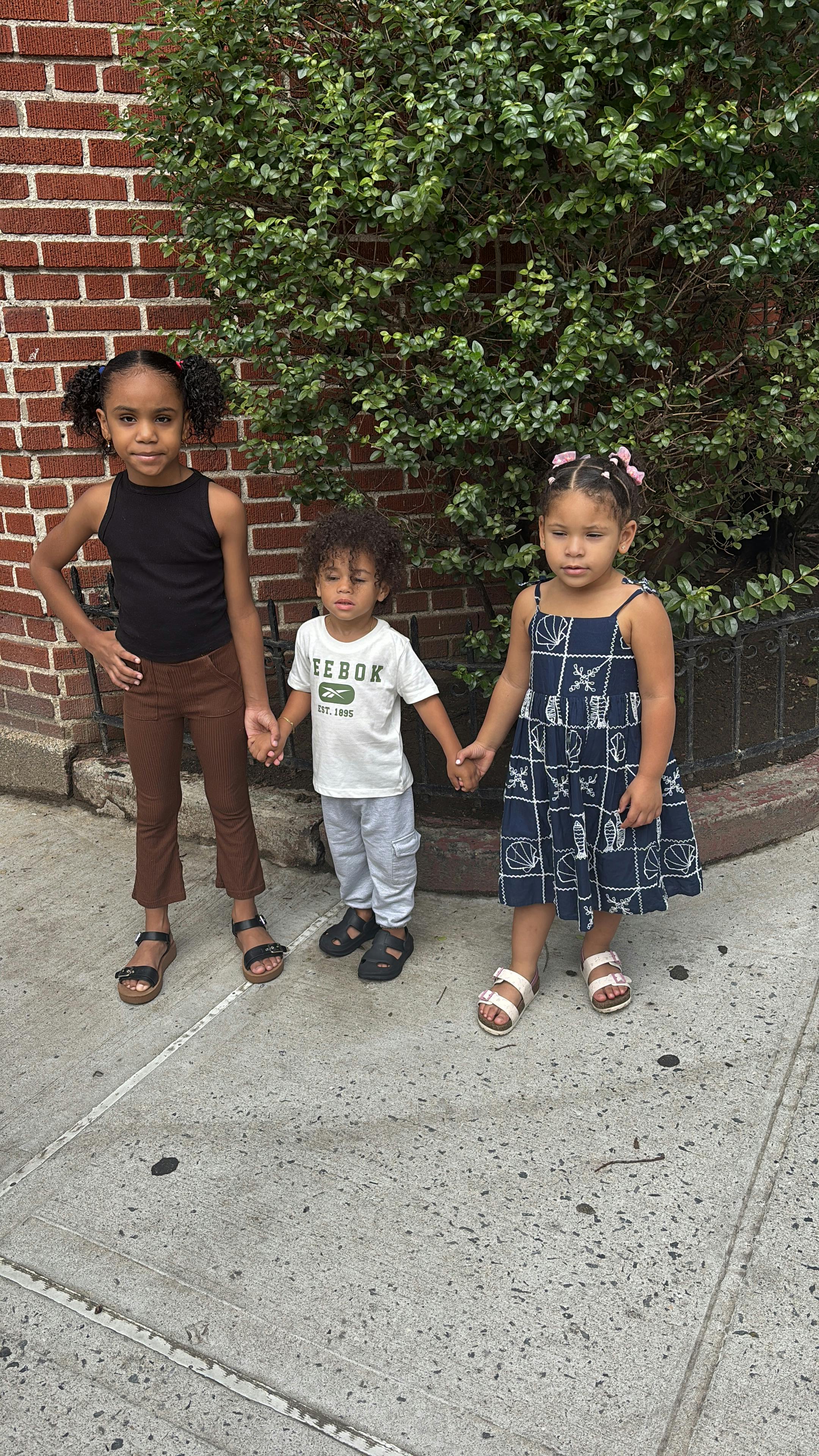 Three children holding hands standing on a sidewalk