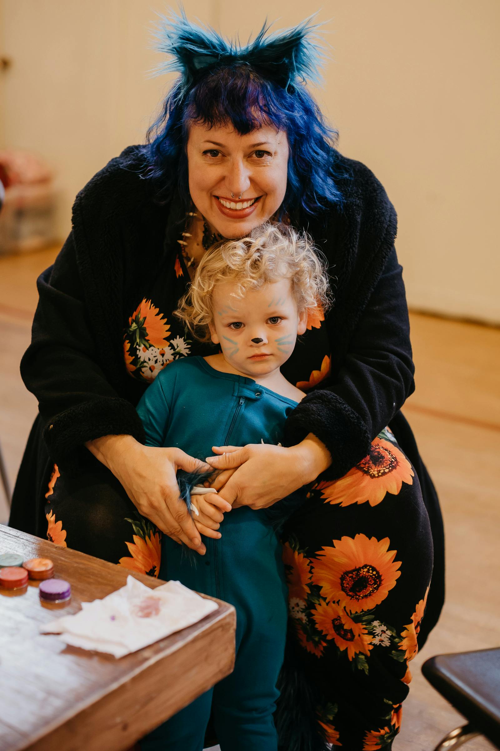 Person with blue hair and cat ears holding a child with face paint