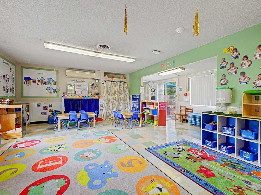 Colorful preschool classroom with tables, chairs, and two large play rugs