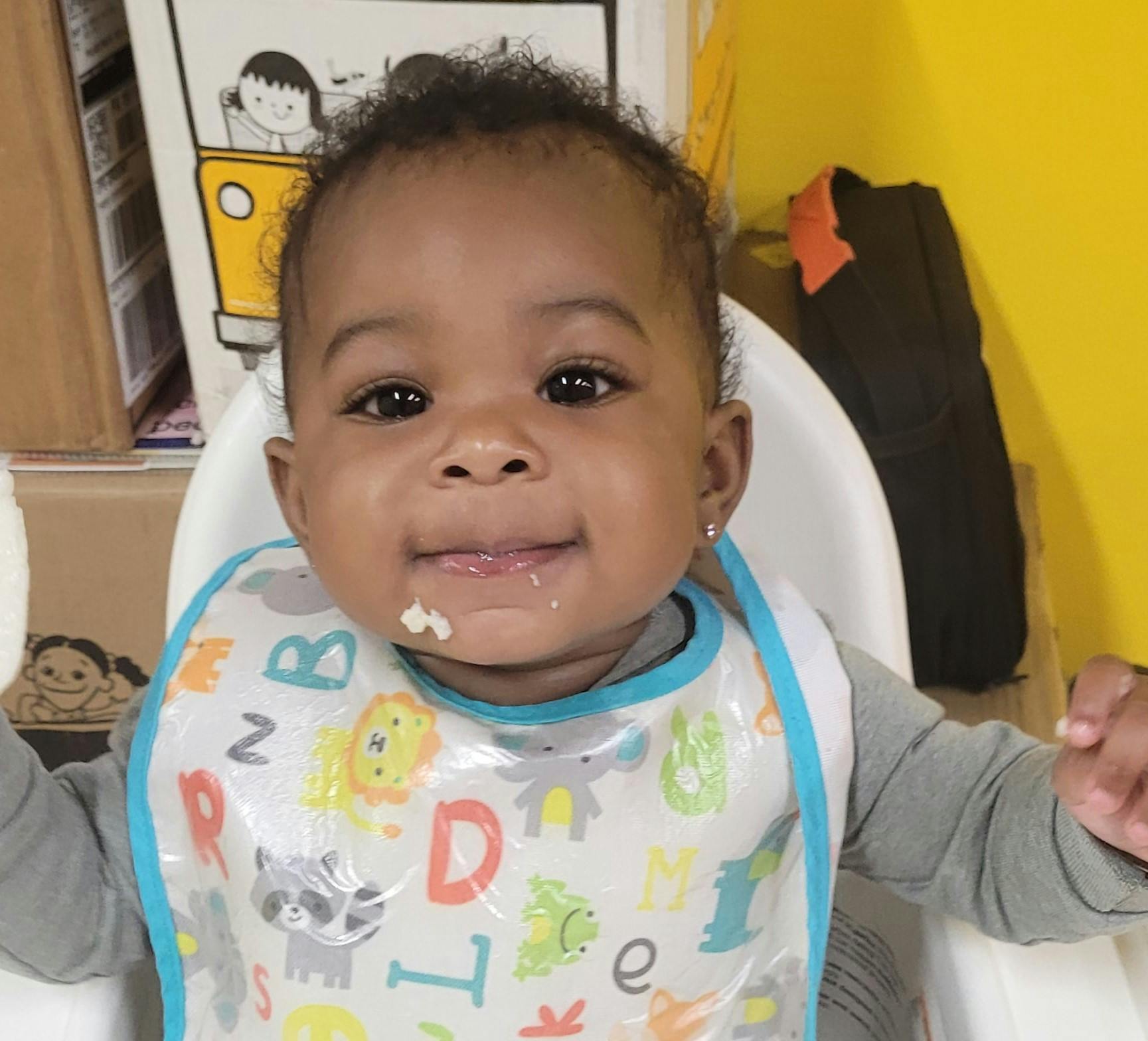 Child in a high chair wearing a bib with food on their face