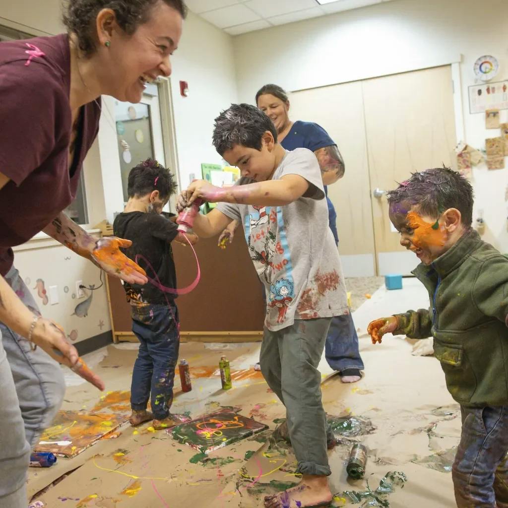 Adult and children covered in paint playing in a classroom