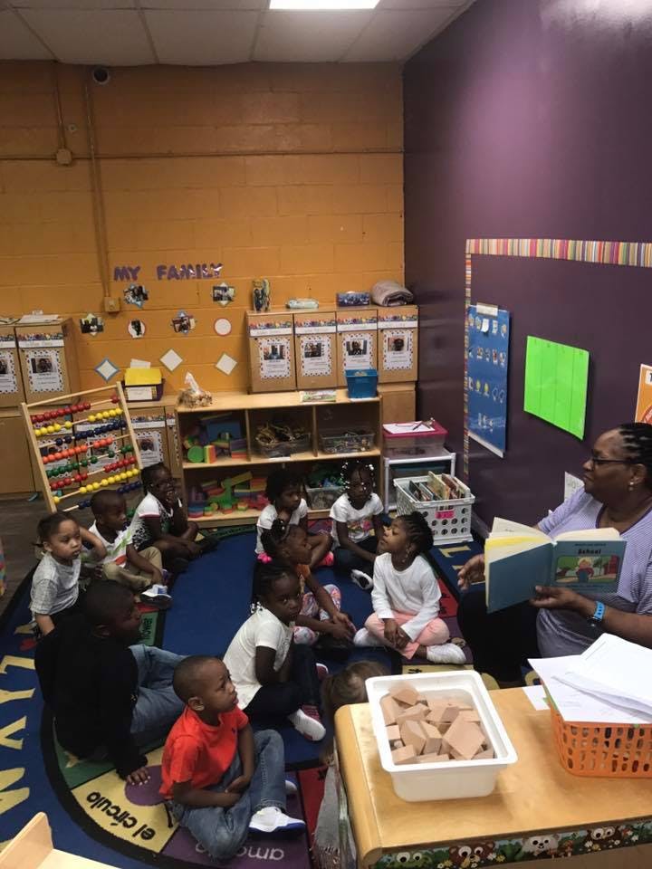 Adult reading a book to a group of children in a classroom