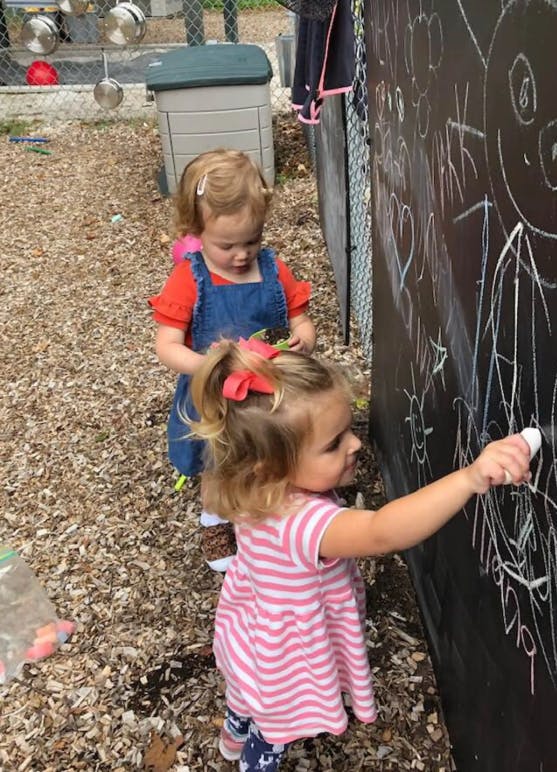 Two children drawing on a chalkboard outdoors