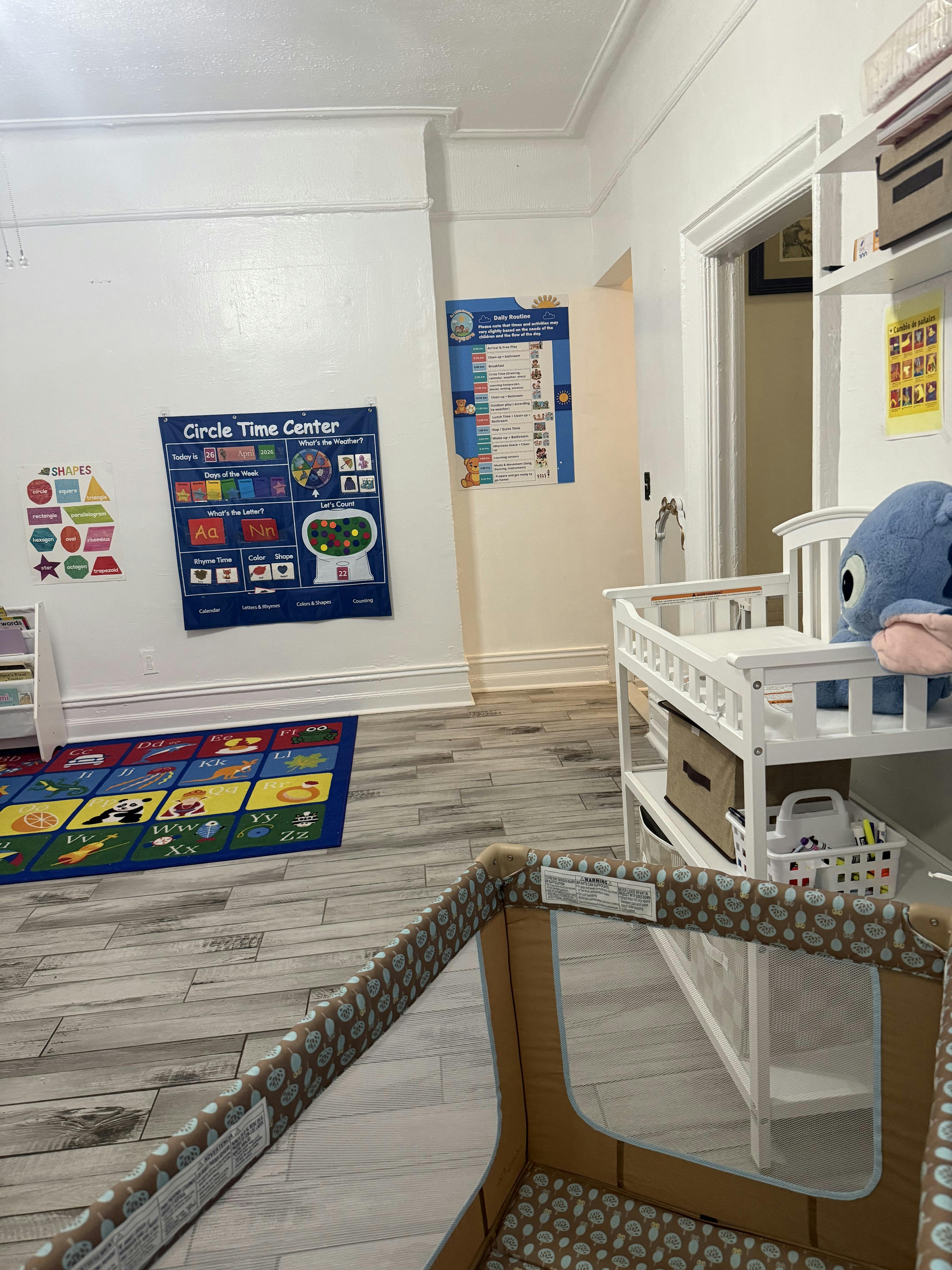 Childcare room with a playpen, changing table, and educational wall posters
