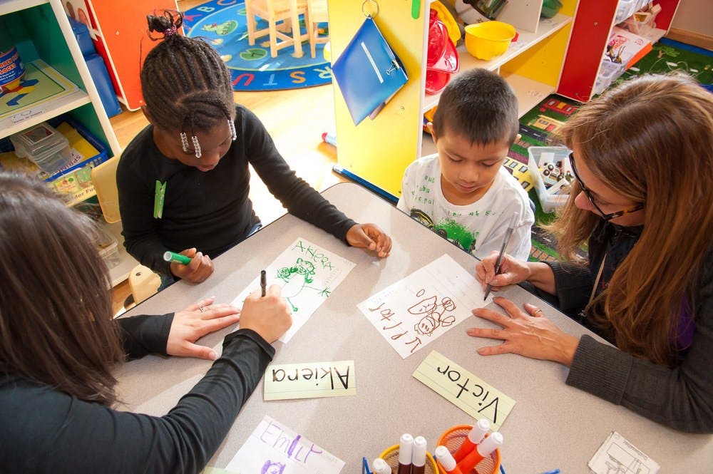 Two adults and two children drawing at a table in a classroom