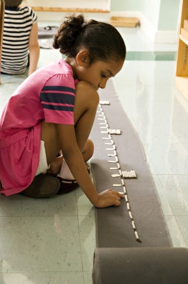 Child kneeling on floor, arranging small pieces on a long mat