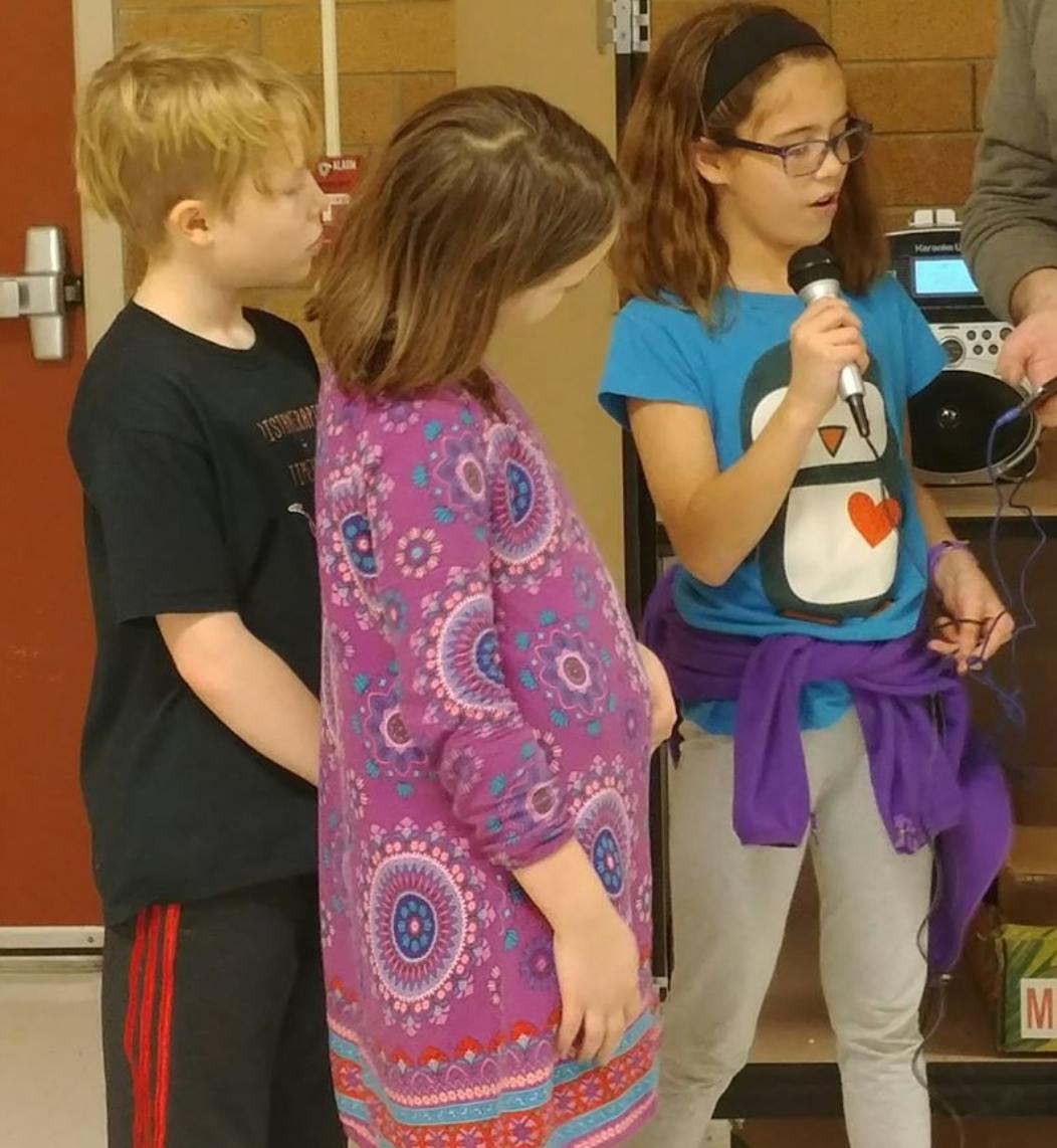 Child speaking into a microphone with two other children nearby